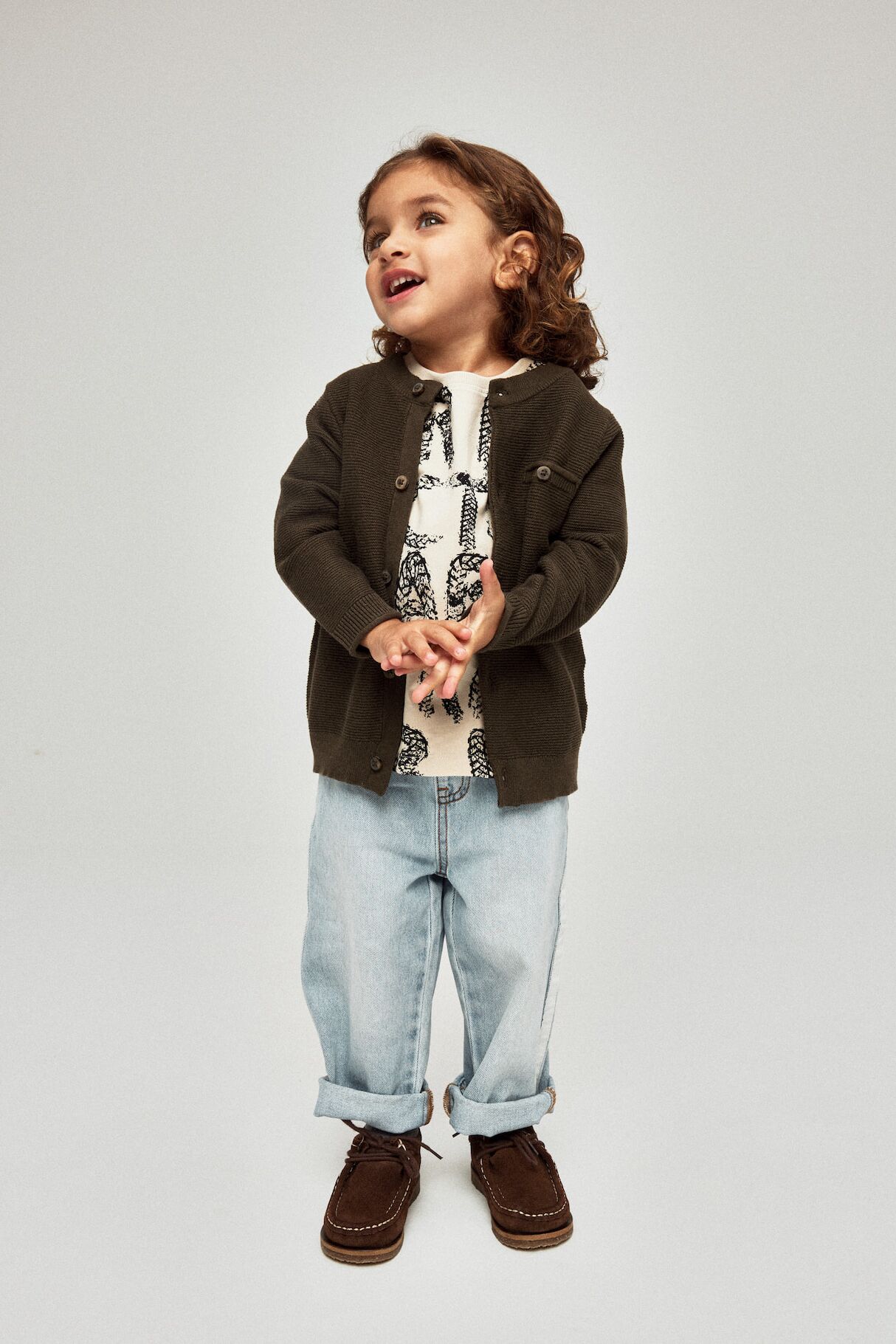 Kleines Mädchen in hochgekrempelter Jeans, T-Shirt und Jacke von name it blickt nach oben