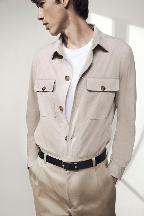 Männliches Modell in beiger Chinohose, weißem Shirt und beigen Overshirt von BOSS blickt lässig zur Seite