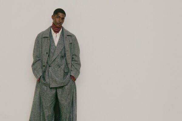 Männliches Model in grauer Hose, Grauen Jackett und grauen Mantel von GANT posiert mit Händen in den Hosentaschen