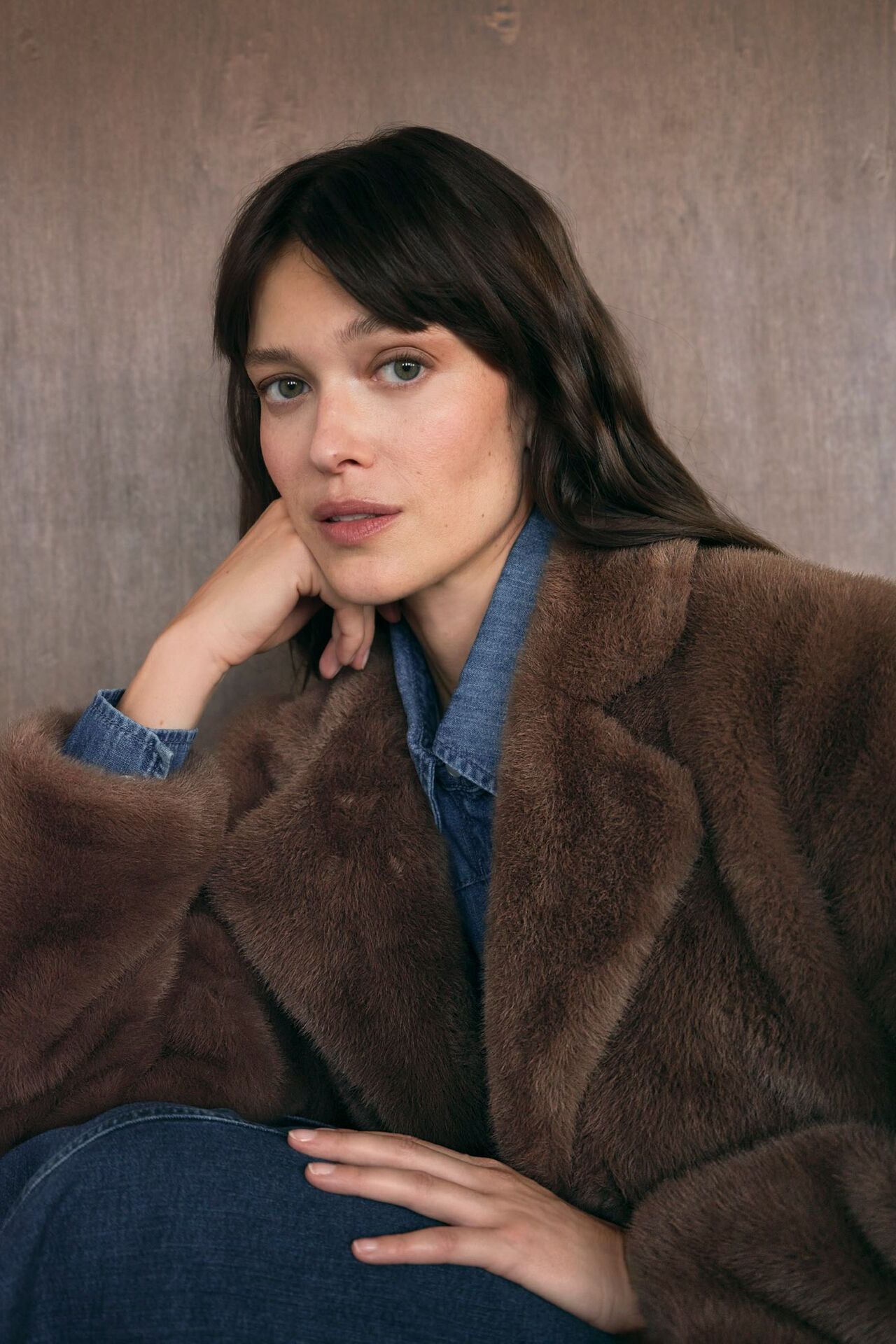 Weibliches Modell in Jeans-Bluse und brauner Felljacke stützt Ihren Kopf auf der Hand ab