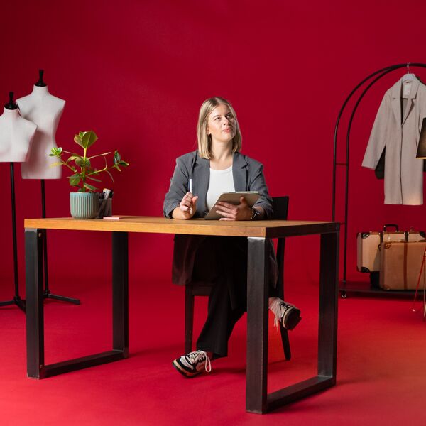 Eine Frau sitzt an einem Tisch vor einem roten Hintergrund.