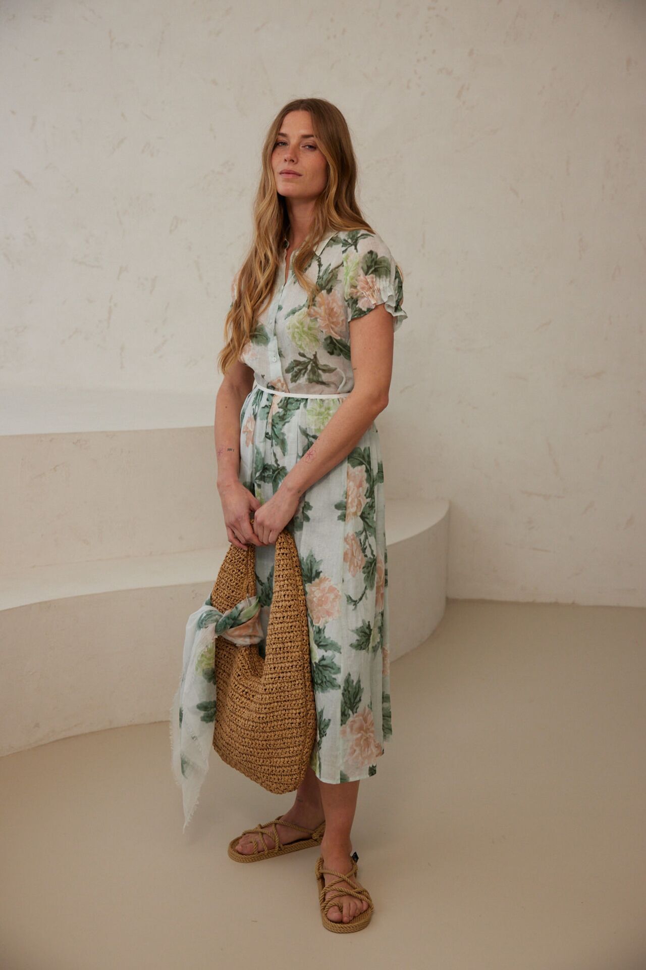 Weibliches Modell in Maxi-Rock und Hemdbluse mit Floralprint hält eine Strandtasche