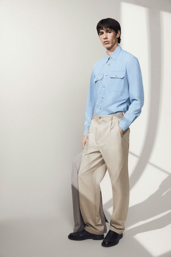 Männliches Model in beiger Hose und hellblauen Hemd von BOSS hält ein graues Sakko in der Hand