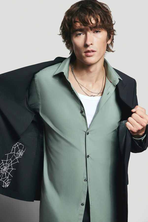 Männliches Modell in hellgrünem Hemd und schwarzen Sakko von BOSS zieht sich das Sakko aus