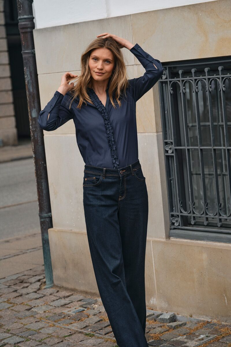 Weibliches Modell in Dunkelblauer JEans und Dunkelblauer Satinbluse richtet sich die Haare