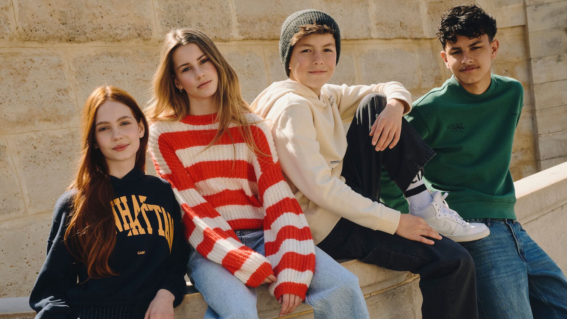 Gruppe von Teenies in cooler Kindermode von Garcia posieren auf einer Mauer