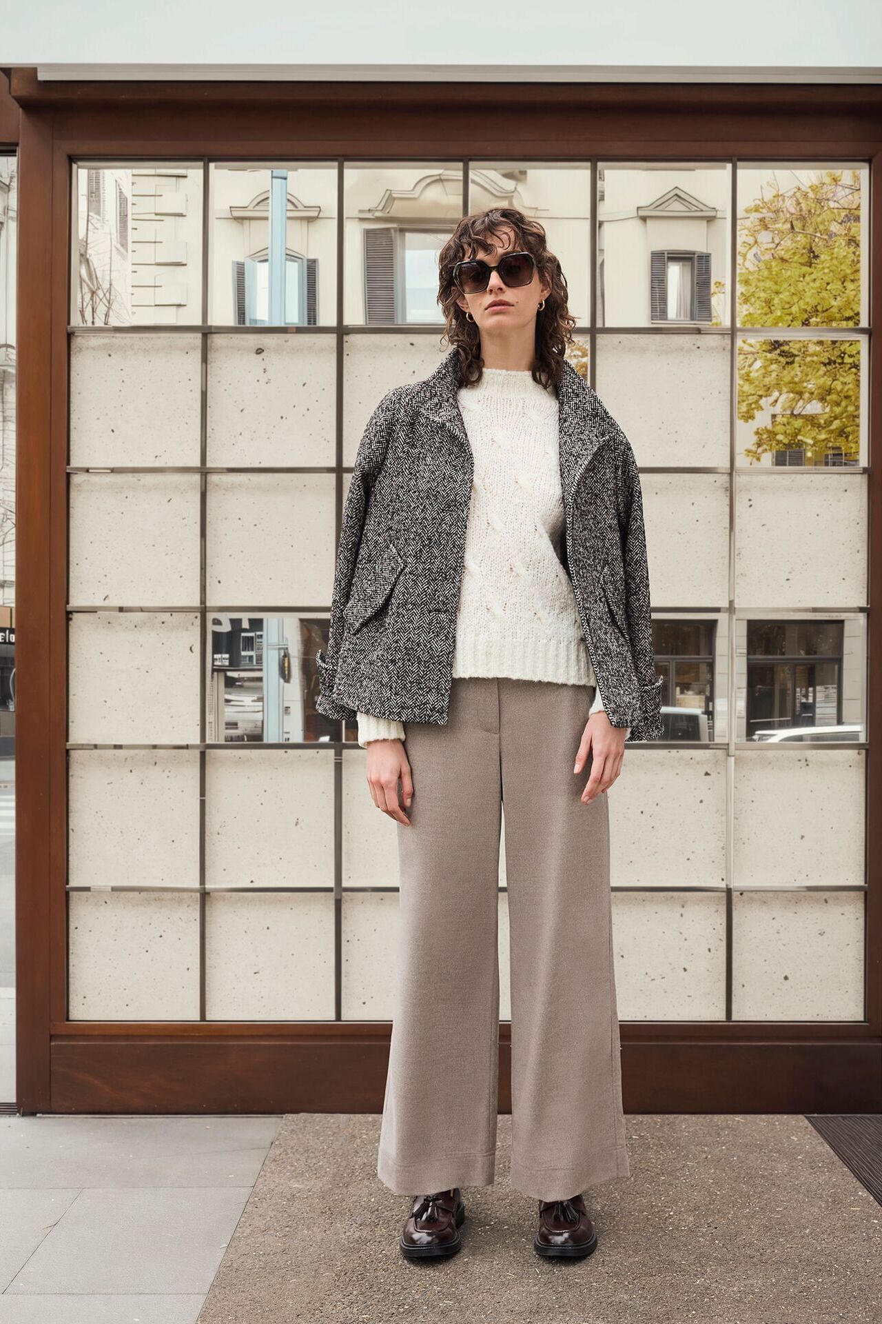 Weibliches Modell in grau-schwarzer Wolljacke von CINQUE posiert vor einem Schaufenster