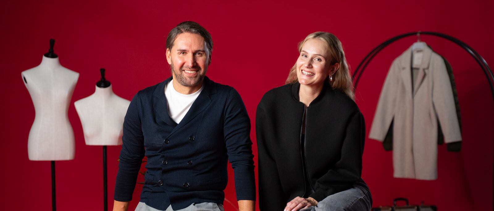 Ein Mann und eine Frau posieren für ein Foto vor einem roten Hintergrund.