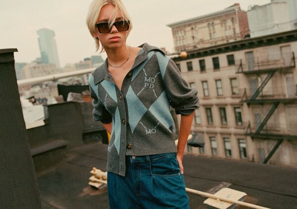 Weibliches Model in blauer Ballon-Jeans und gemusterten Strickjacke von Marc O Polo Denim auf einem Hochhausdach