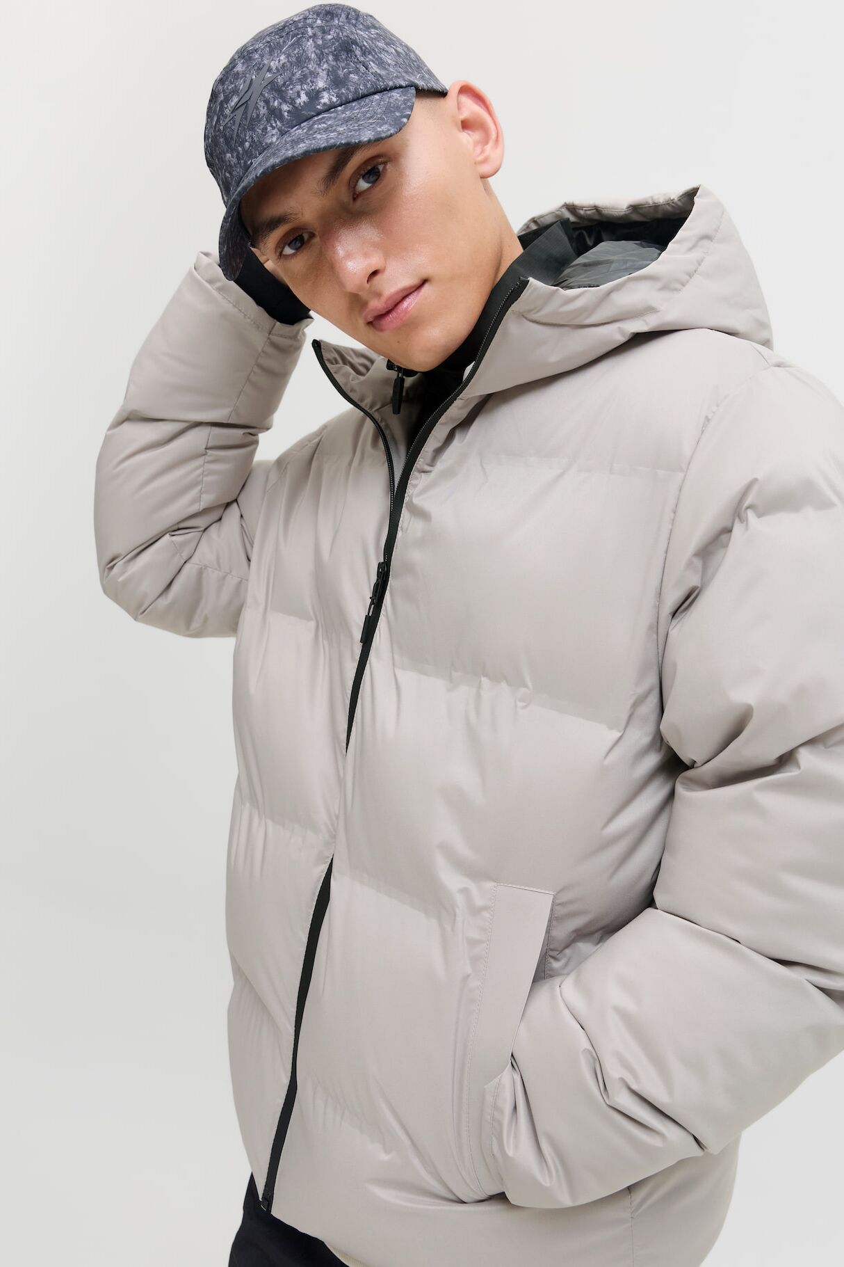 Männliches Modell in silberweisser Steppjacke von Jack & Jones fässt sich an den Hinterkopf