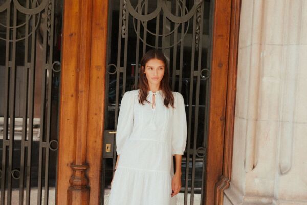 Weibliches Modell in weißen A-Linien Kleid von Vero Moda posiert vor einer großen Eingangstür