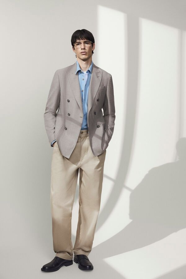 Männliches Model in beiger Anzughose, hellblauen Hemd und grauem Sakko von BOSS posiert mit beiden Händen in der Hosentasche