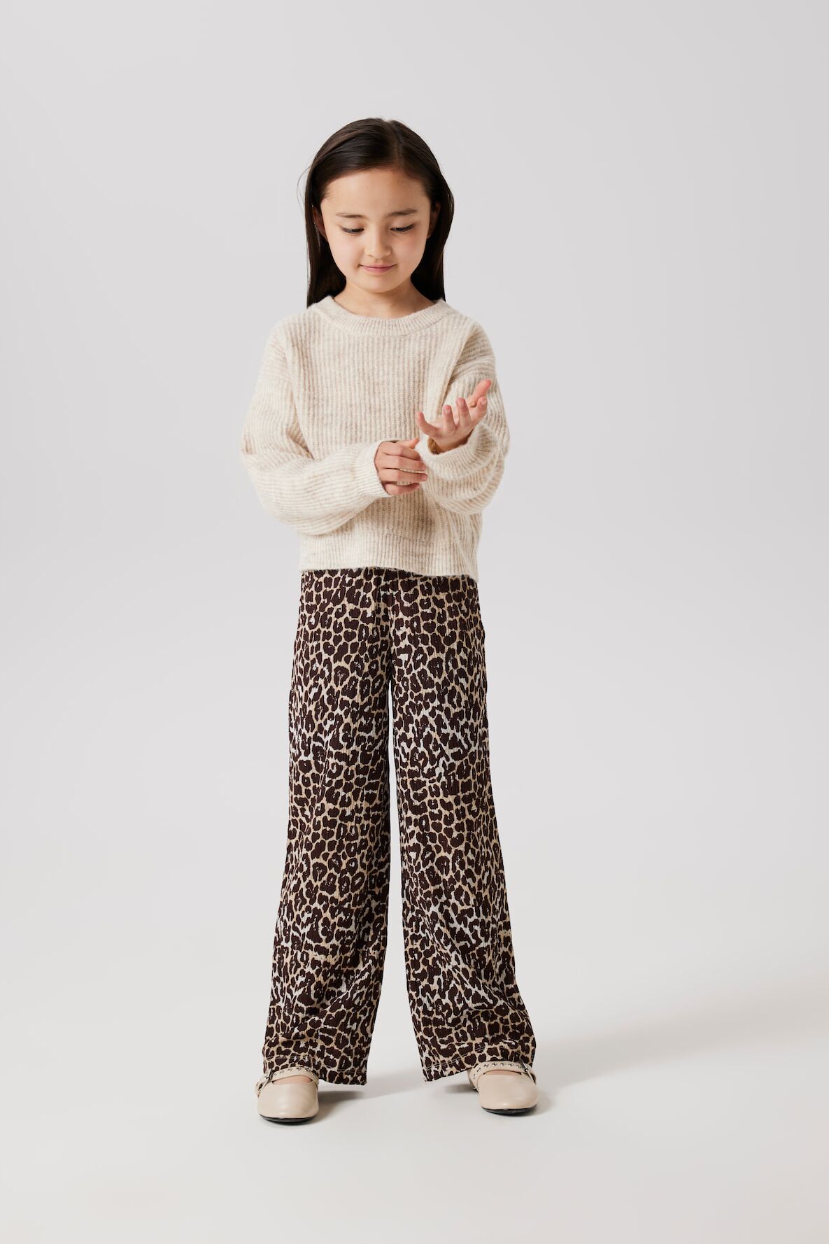 Kleines Mädchen in Leoprint-Hose und beigen Strickpullover von name it krempelt sich die Ärmel hoch