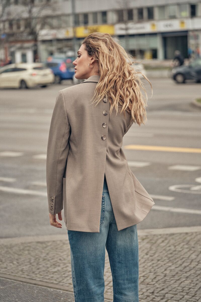 Weibliches Modell in blauer Jeans und beigen Business-Blazer steht auf dem Gehweg