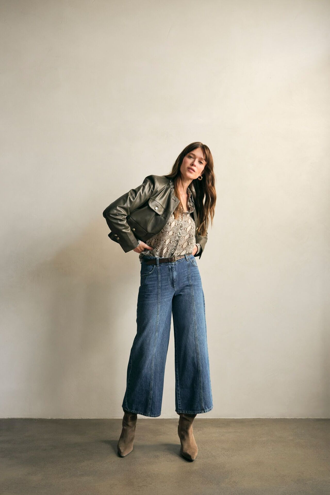 Weibliches Modell in 3/4 Denim , gemusterten Bluse und Lederjacke zupft an ihrer Kleidung