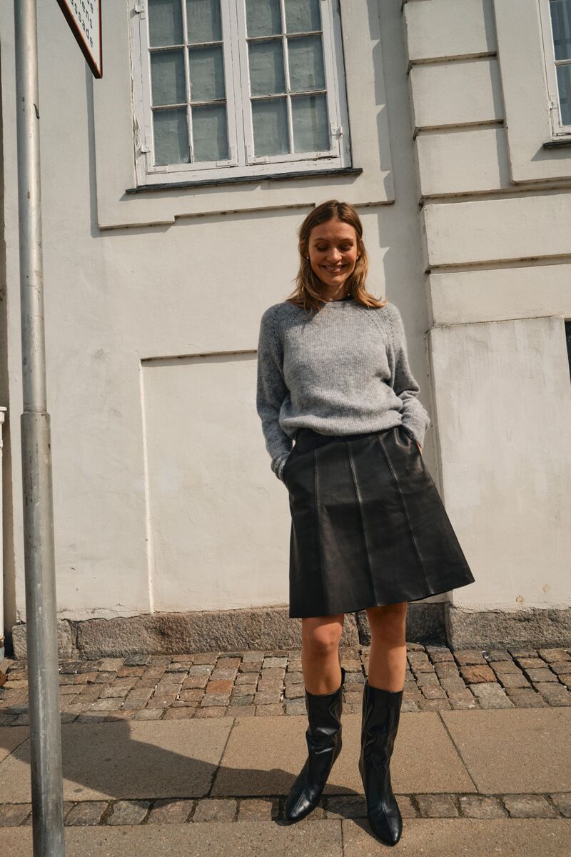 Weibliches Modell in modernen Business-Outfit aus Rock und Strickpullover posiert mit den Händen in der Tasche