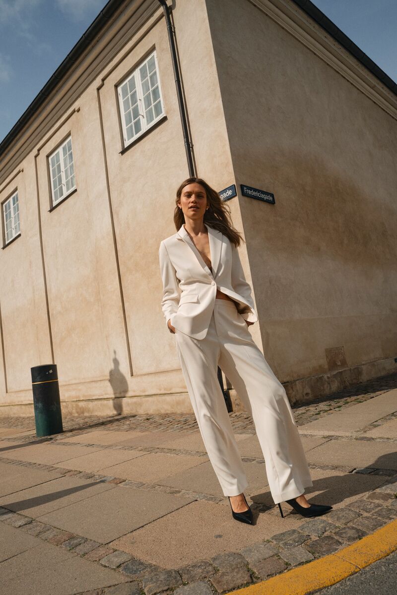 Weibliches Modell in cremeweissen Business Hosenanzug von Mos Mosh posiert vor einem Gebäude