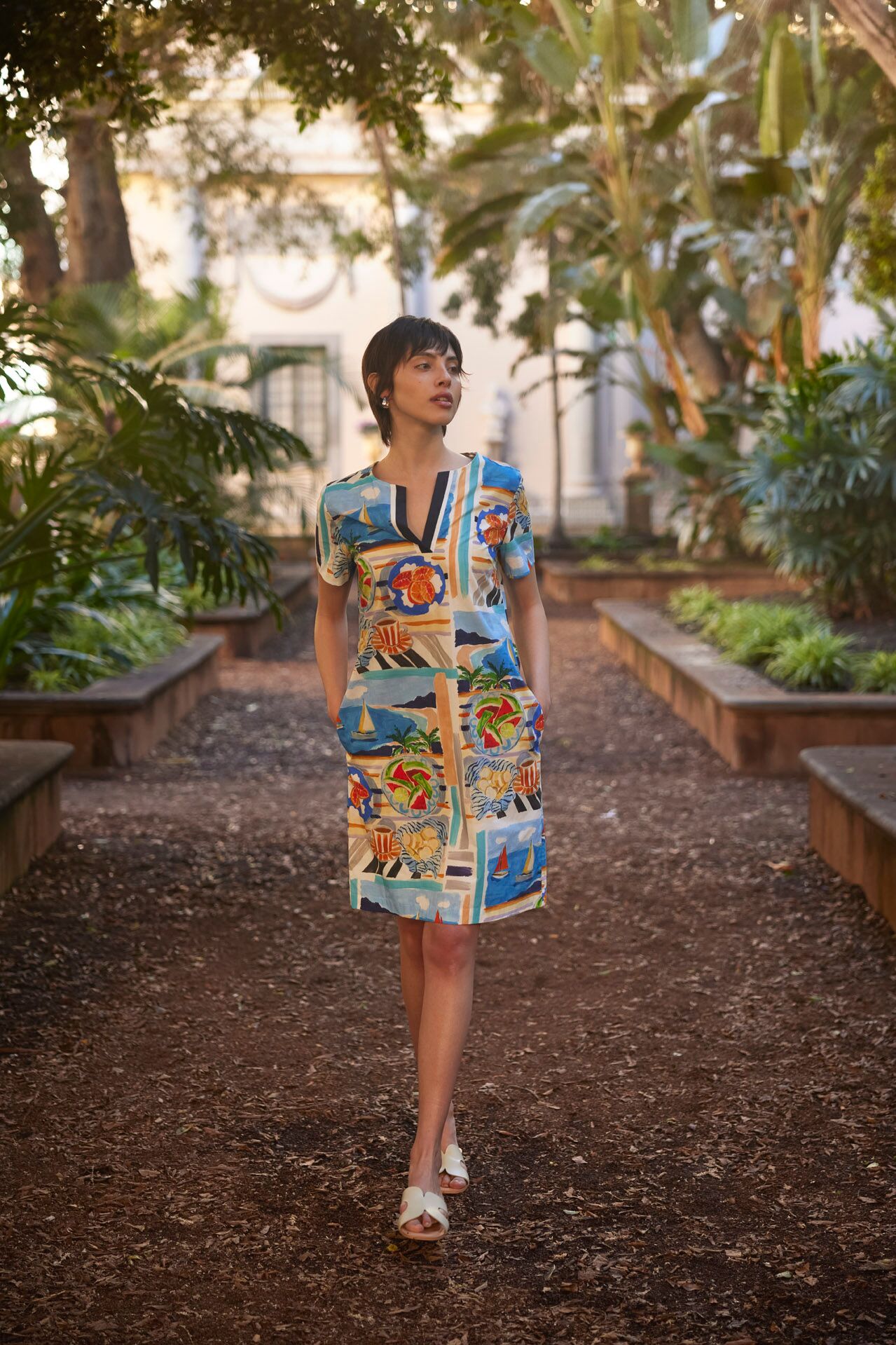 Weibliches Modell in bunten Kleid mit Musterprint und weißen Sandaletten läuft in einem botanischen Garten