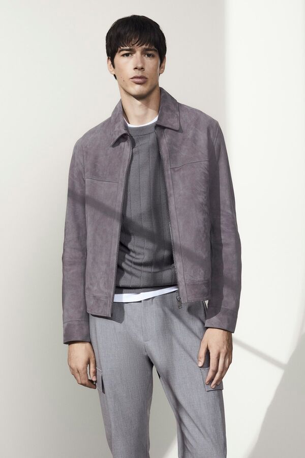 Männliches Modell in hellgrauer Chinohose, dunkelgrauen Pullover und grauen Blousonjacke von BOSS posiert selbstbewusst