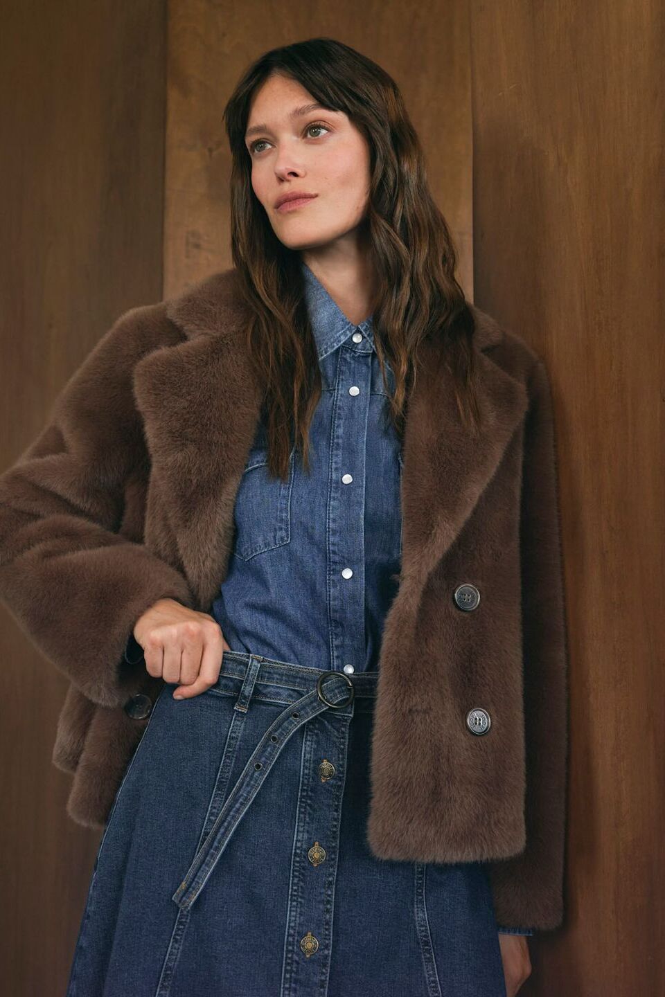 Weibliches Modell in schicker Premium-Damenmode posiert vor einer Holzwand