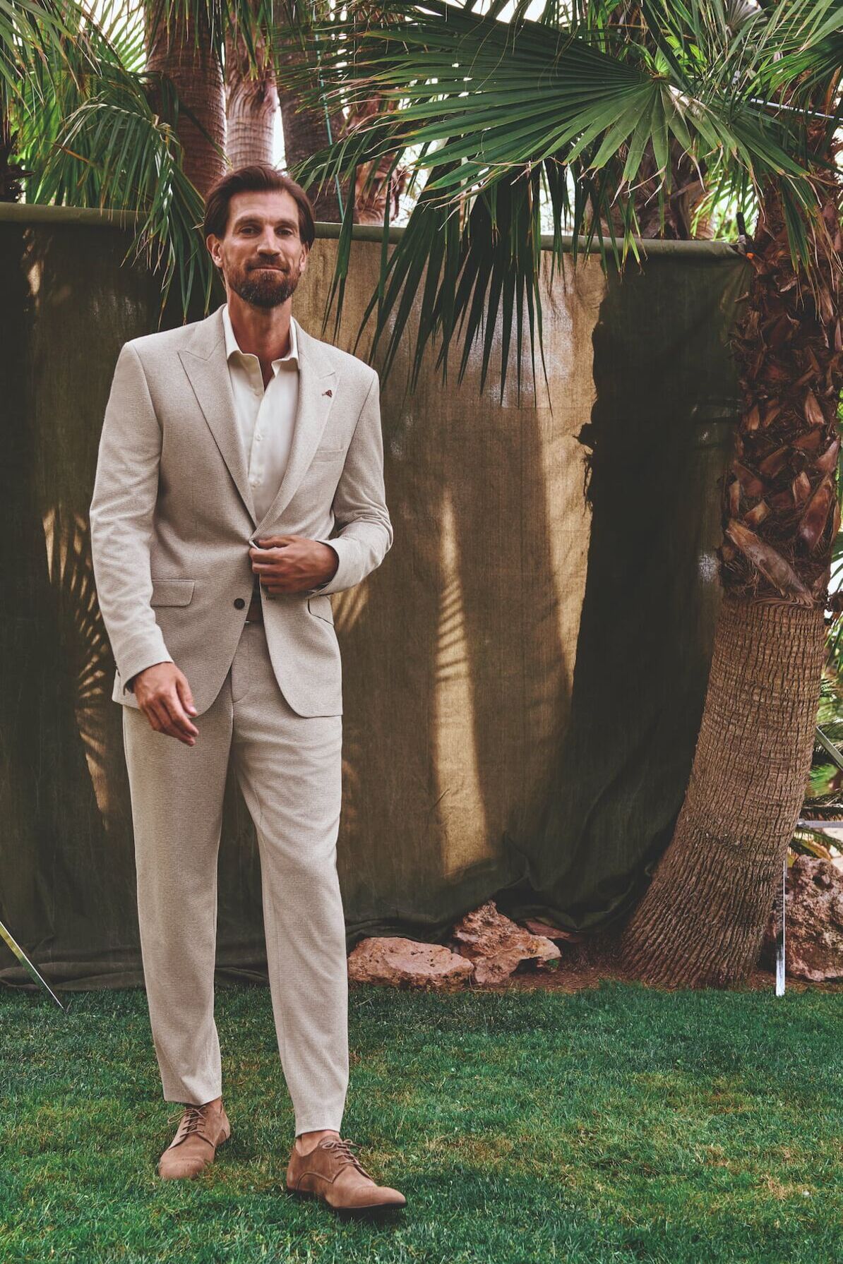 Männliches Modell in hellbeigen Anzug von Roy Robson posiert in einem Garten