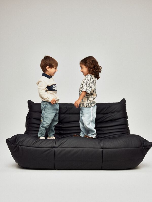 Zwei Kinder in moderner Kindermode von name it stehen sich auf einem Sofa gegenüber