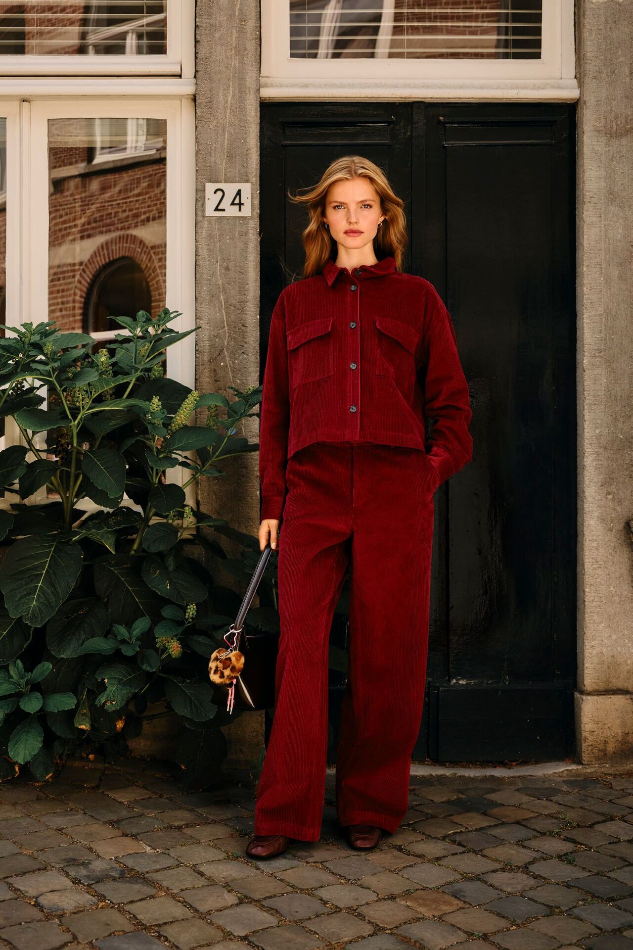 Weibliches Modell in angesagten All-Over-Cord Look in Dunkelrot posiert lässig mit einer Hand in der Hosentasche