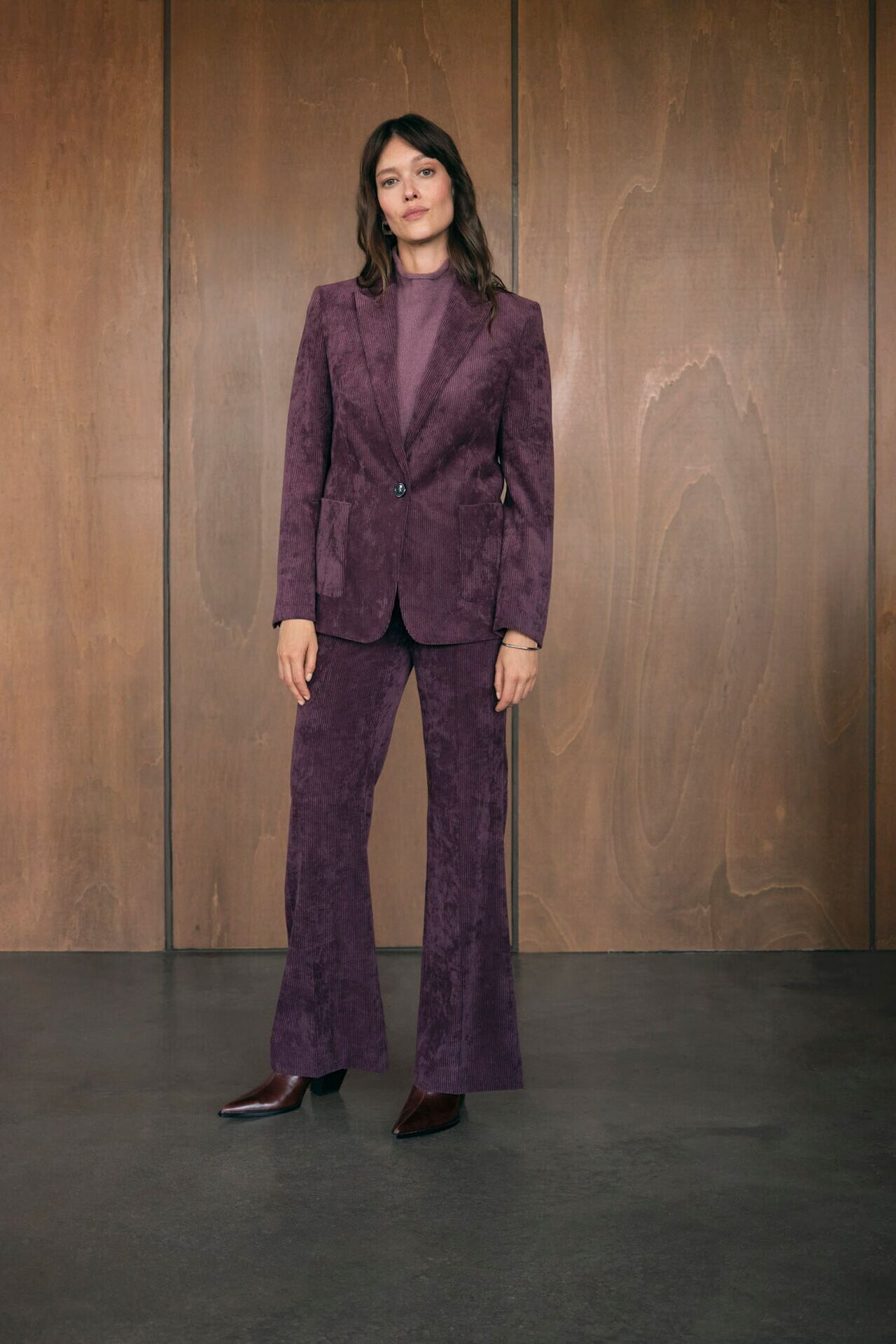 Weibliches Modell in lila-roten Cord Hosenanzug von Luisa Cerano posiert selbstbewusst in einem Büro