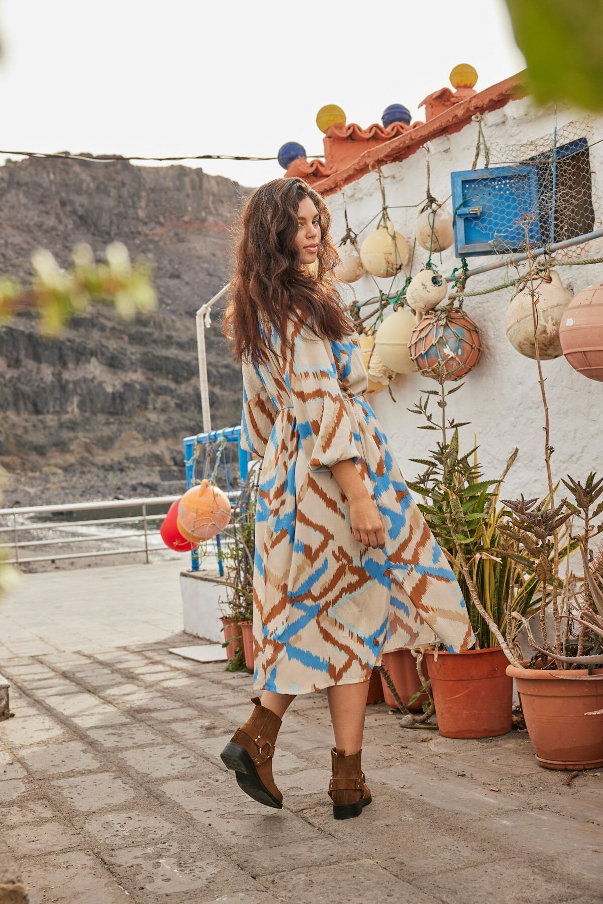 Weibliches Plus Size Modell in gemusterten Kleid von ONLY Carmakoma posiert verspielt vor einem kleinen Häusschen