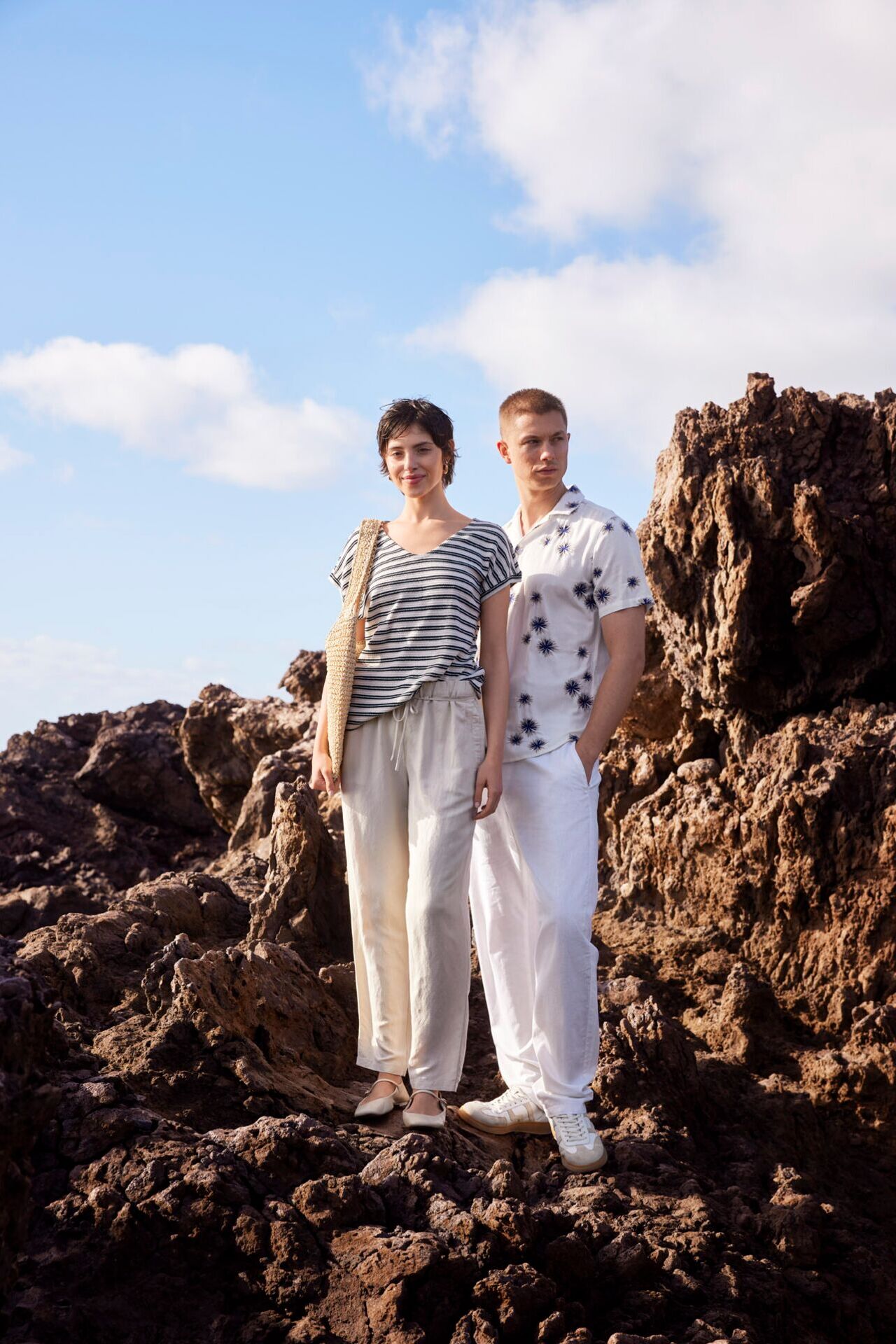 Weibliches und männliches Modell in lässigen Sommer-Outfits von ZINSER posieren auf einem Felsvorsprung
