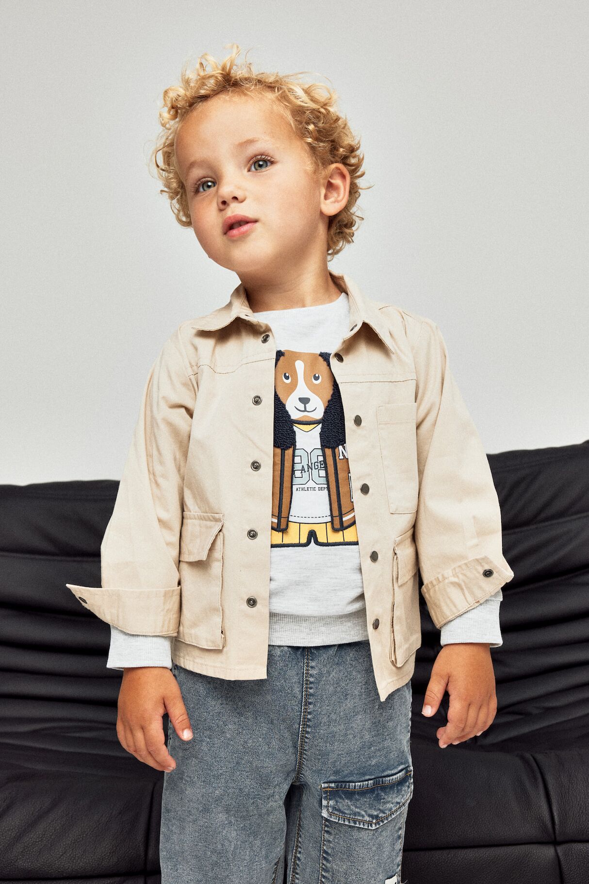 Kleiner Junge in cooler Kindermode von name it steht auf einem Sofa