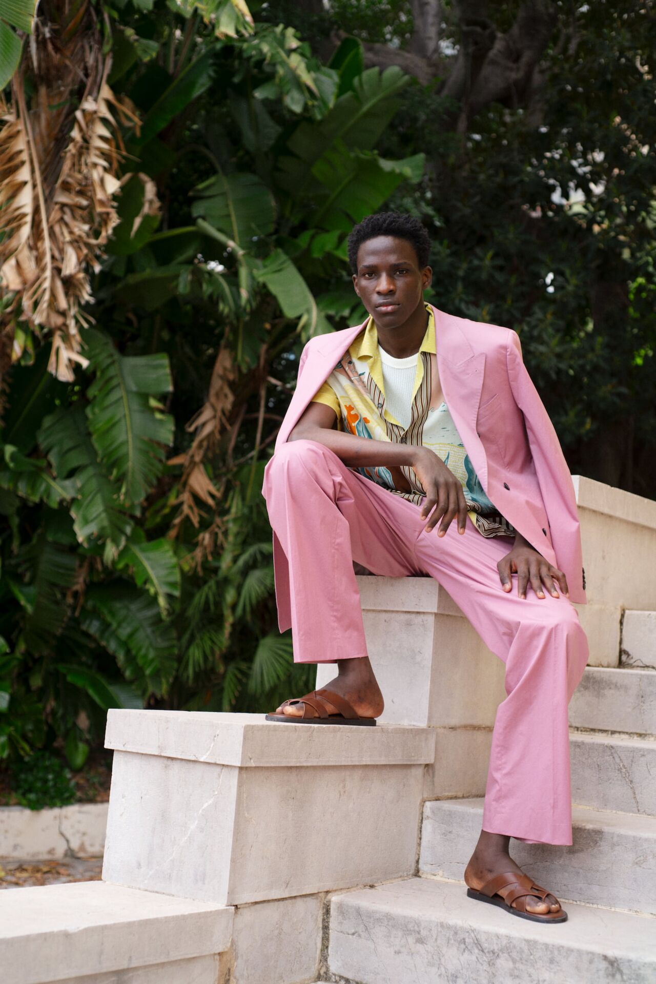 Männliches Modell in einem pinken Anzug von Baldessarini sitzt auf einem Stein