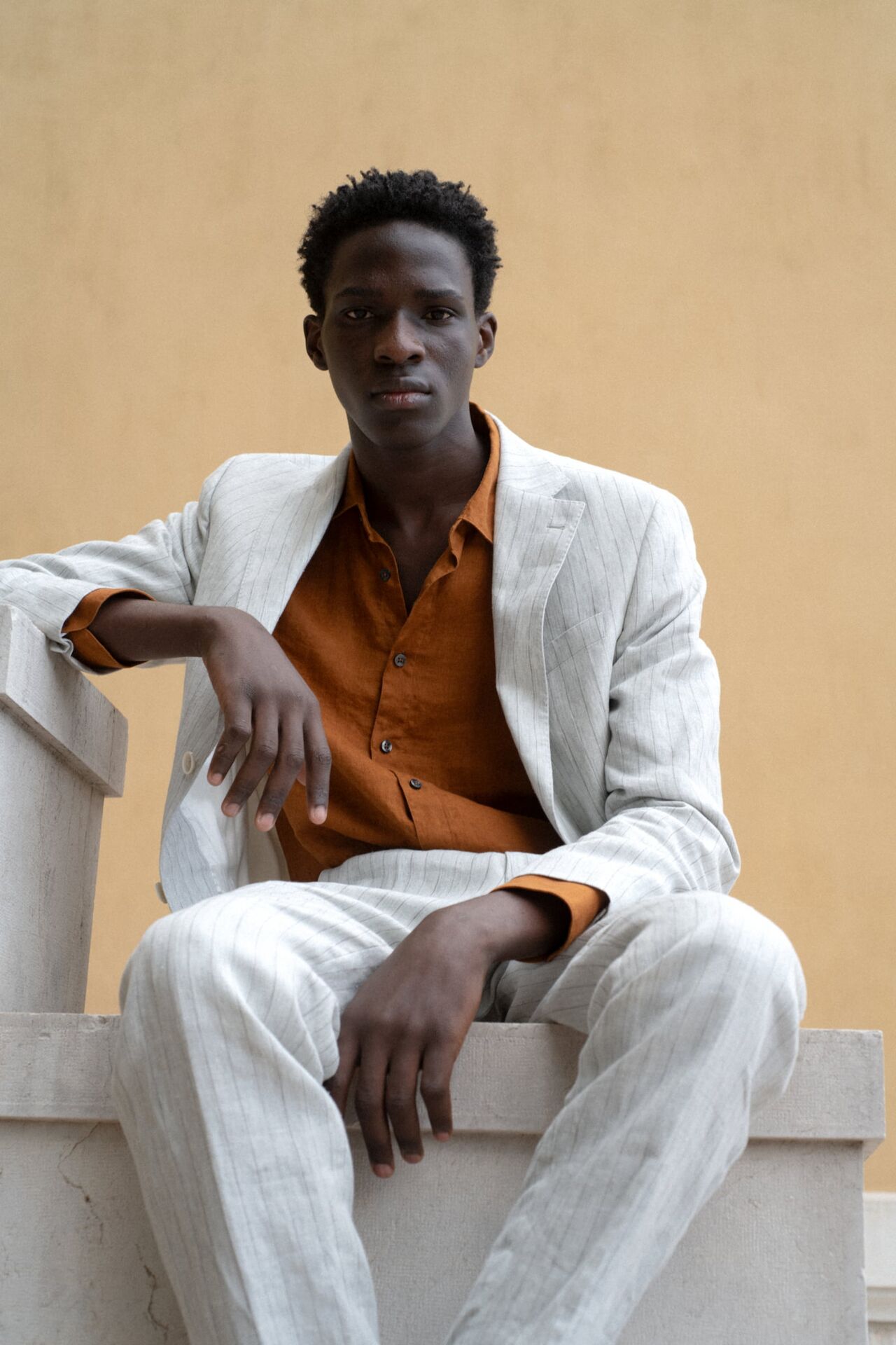 Männliches Modell in braunem Hemd und grauen Anzug von Baldessarini posiert lässig auf einem Steinpodest